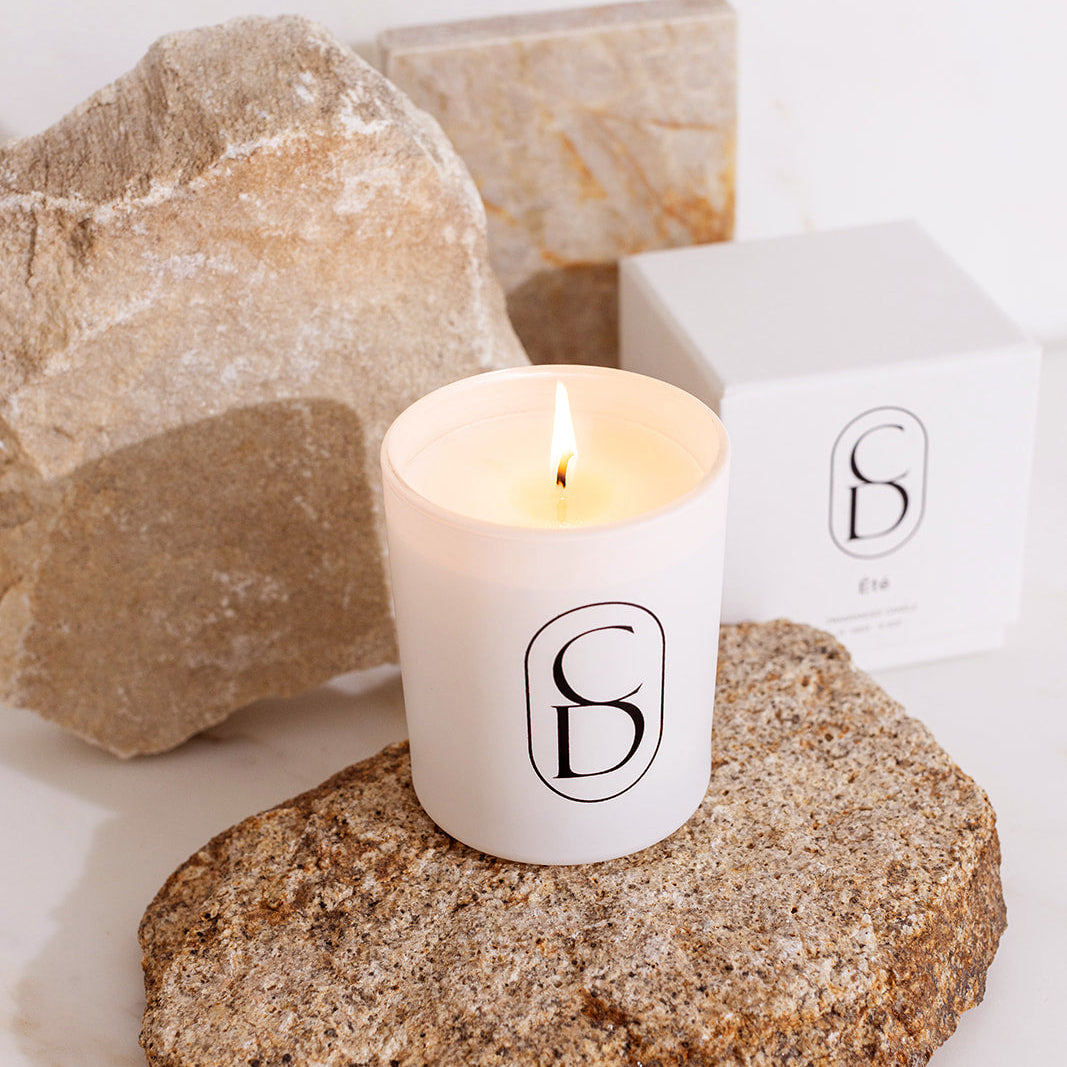 Candle with a logo on a rock next to decorative stones and a box
