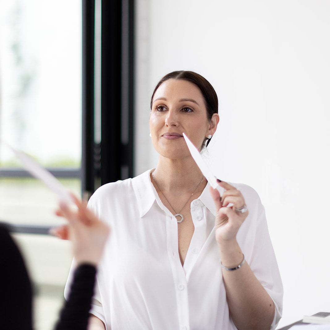 Woman in a white shirt holding a piece of paper, possibly an interview scenario.